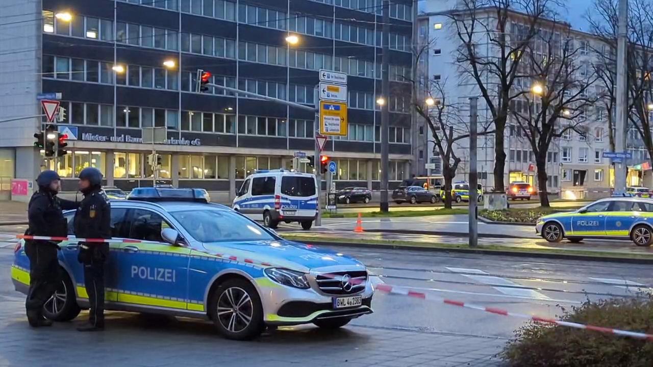 Polizisten stehen an einem Polizeifahrzeug in Karlsruhe. Die Umgebung ist wegen einer Geiselnahme abgesperrt. Polizisten stehen an einem Polizeifahrzeug in Karlsruhe. Die Umgebung ist wegen einer Geiselnahme abgesperrt.