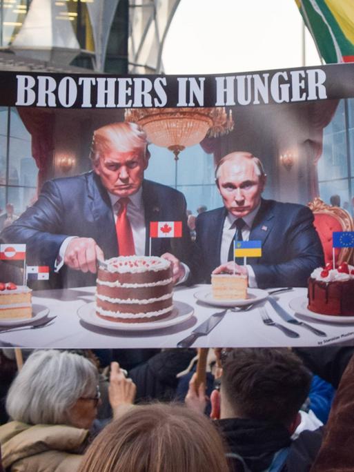 Ein Demonstrant vor der US-Botschaft in London hält im März 2025 ein Plakat hoch, auf dem Trump und Putin Kanada- und Ukraine-Kuchen essen.