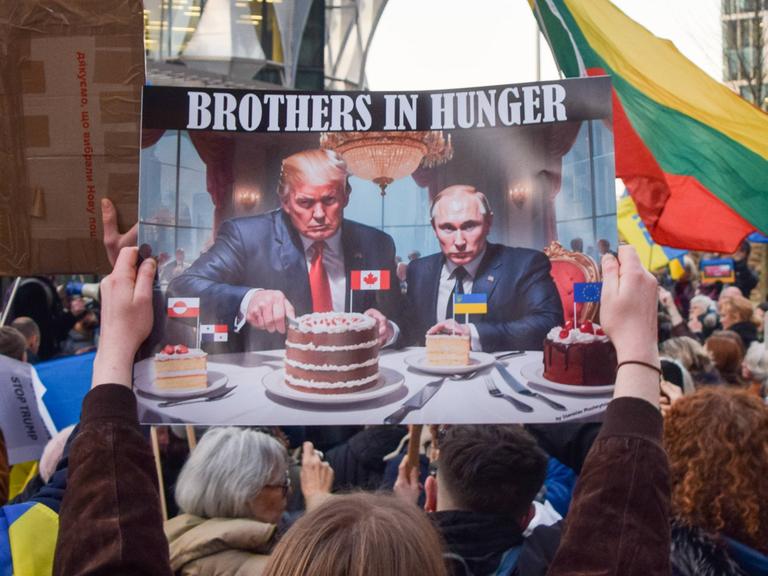 Ein Demonstrant vor der US-Botschaft in London hält im März 2025 ein Plakat hoch, auf dem Trump und Putin Kanada- und Ukraine-Kuchen essen.