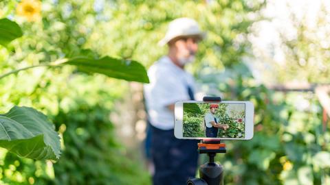 Ein moderner Landwirt filmt sich mit einem Mobiltelefon zwischen Gemüsepflanzen 