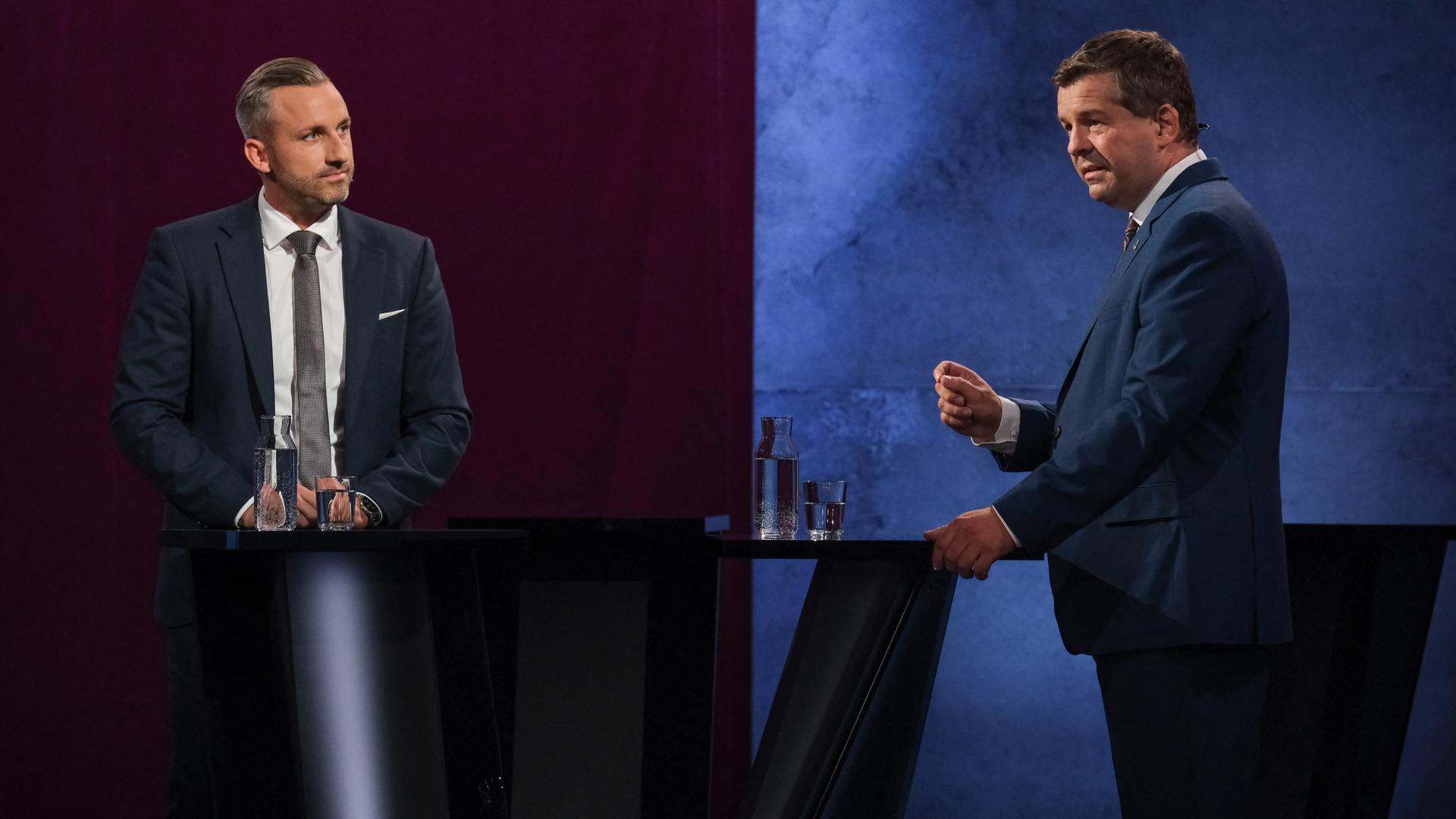 Das Bild zeigt eine Situation aus der Sendung des MDR. Siegmund und Schulze stehen an Redepulten. Schulze spricht und gestikuliert mit einer Hand, Siegmund schaut zu ihm herüber.