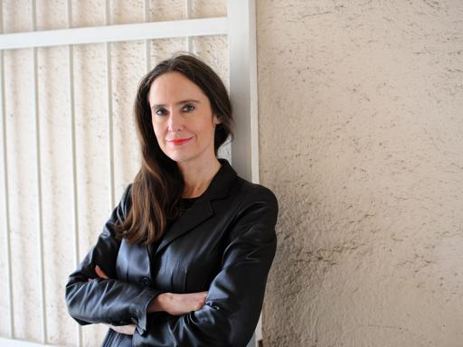 Porträtfoto von Tanja Kinkel. Sie lehnt mit verschrenkten Armen an einer Hauswand mit Toreinfahrt.