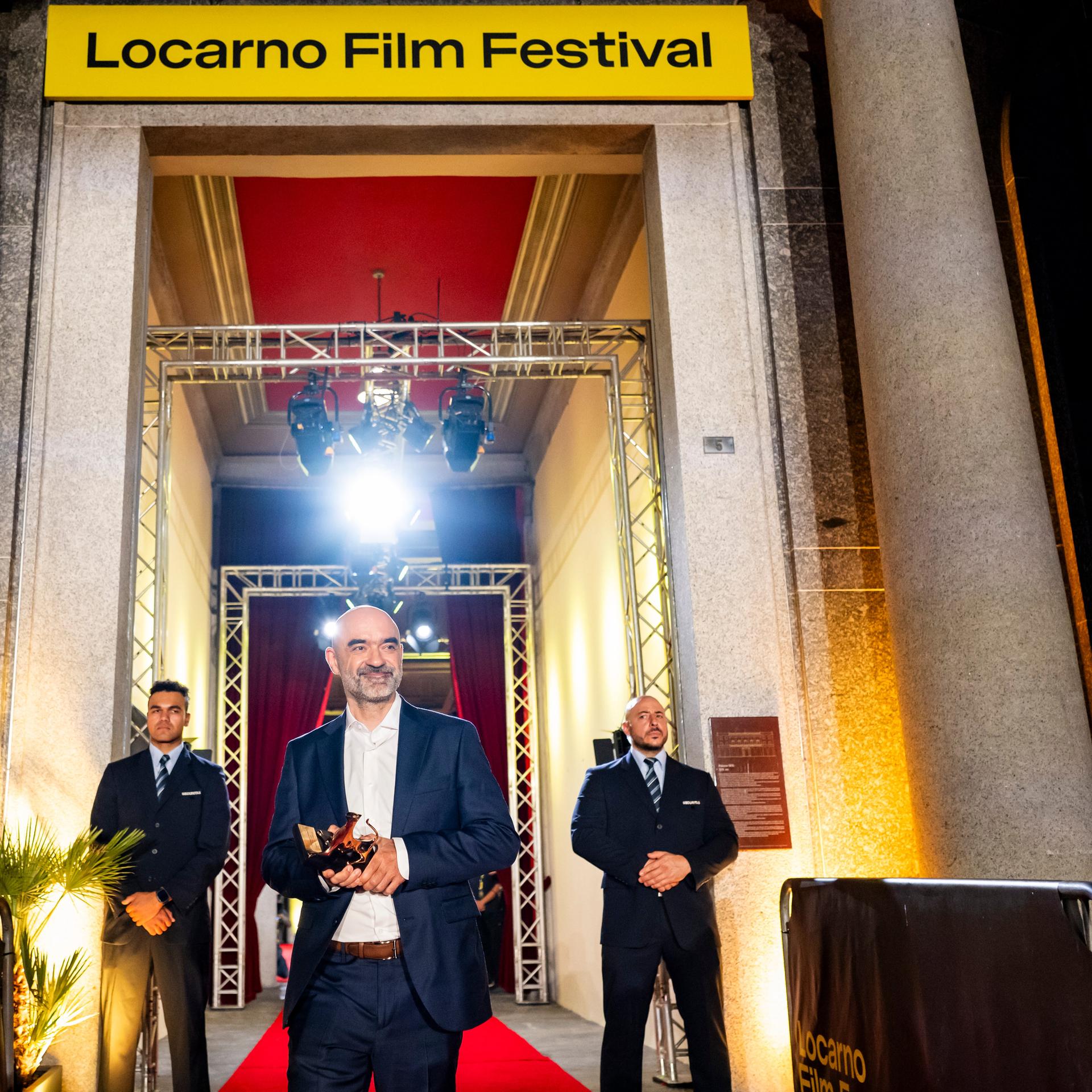 Der Regisseur und Drehbuchautor Florin Șerban steht mit einem Preis in der Hand unter einem Torbogen. Darüber der Schriftzug "Locarno Film Festival"