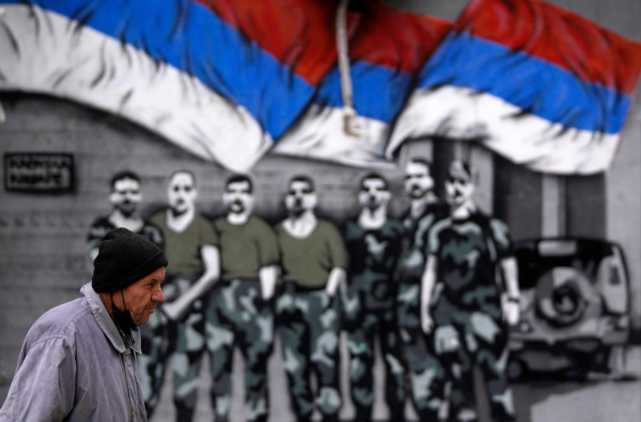 A man walks by graffiti that showing Serbian flags and soldiers in northern, Serb-dominated part of ethnically divided town of Mitrovica, Kosovo, Friday, Oct. 15, 2021. Tensions between Kosovo and Serbia resumed Wednesday after Kosovo police clashed with ethnic Serbs during an anti-smuggling operation. Kosovo, a Serbian province before it declared independence in 2008, was in a war in 1998-1999 between Serbian troops and ethnic Albanian separatists fighting for independence until a NATO air campaign pushed Serb forces away. (AP Photo/Darko Vojinovic)