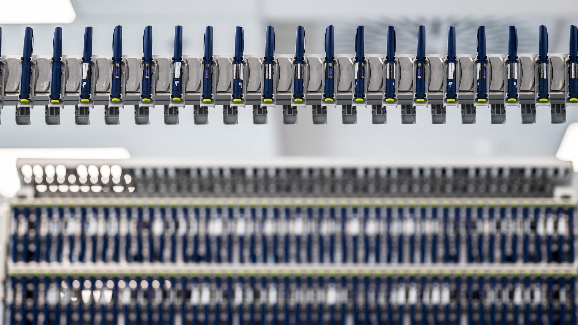 In einer Fabrik werden Abnehmspritzen der Marke Ozempic produziert. Die dunkelblauen Spritzen, die die Form von Stiften haben, sind aufgereiht in einer Produktionskette. Im Hintergrund sind noch mehr.