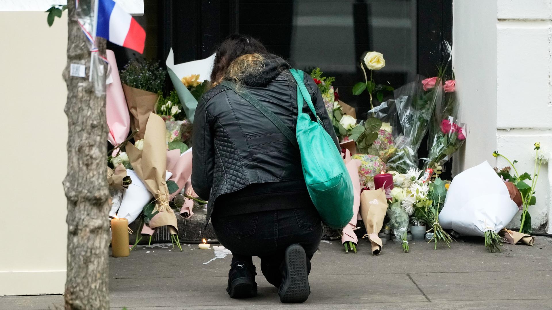 Eine Frau kniet vor dem Konzertsaal Bataclan in Paris. Viele Blumen sind im Eingangsbereich. Eine Frau kniet vor dem Konzertsaal Bataclan in Paris. Viele Blumen sind im Eingangsbereich.