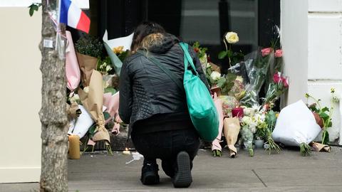 Eine Frau kniet vor dem Konzertsaal Bataclan in Paris. Viele Blumen sind im Eingangsbereich. 