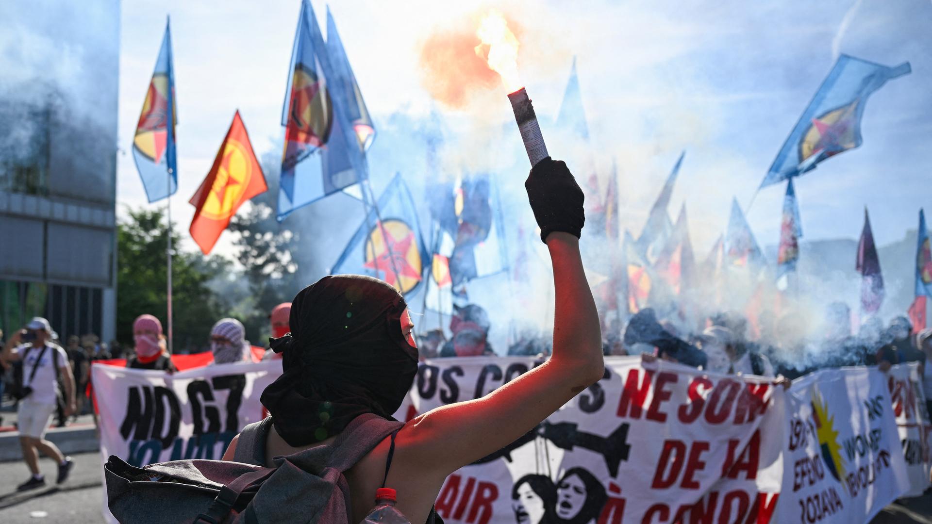 Ein vermummter Demonstrant reckt eine brennende Fackel in die Höhe. Dahinter laufen weitere Teilnehmer der Proteste. Sie halten ein Banner mit der Aufschrift "NoG7", dem Motto der Veranstaltung. Ein vermummter Demonstrant reckt eine brennende Fackel in die Höhe. Dahinter laufen weitere Teilnehmer der Proteste. Sie halten ein Banner mit der Aufschrift "NoG7", dem Motto der Veranstaltung.