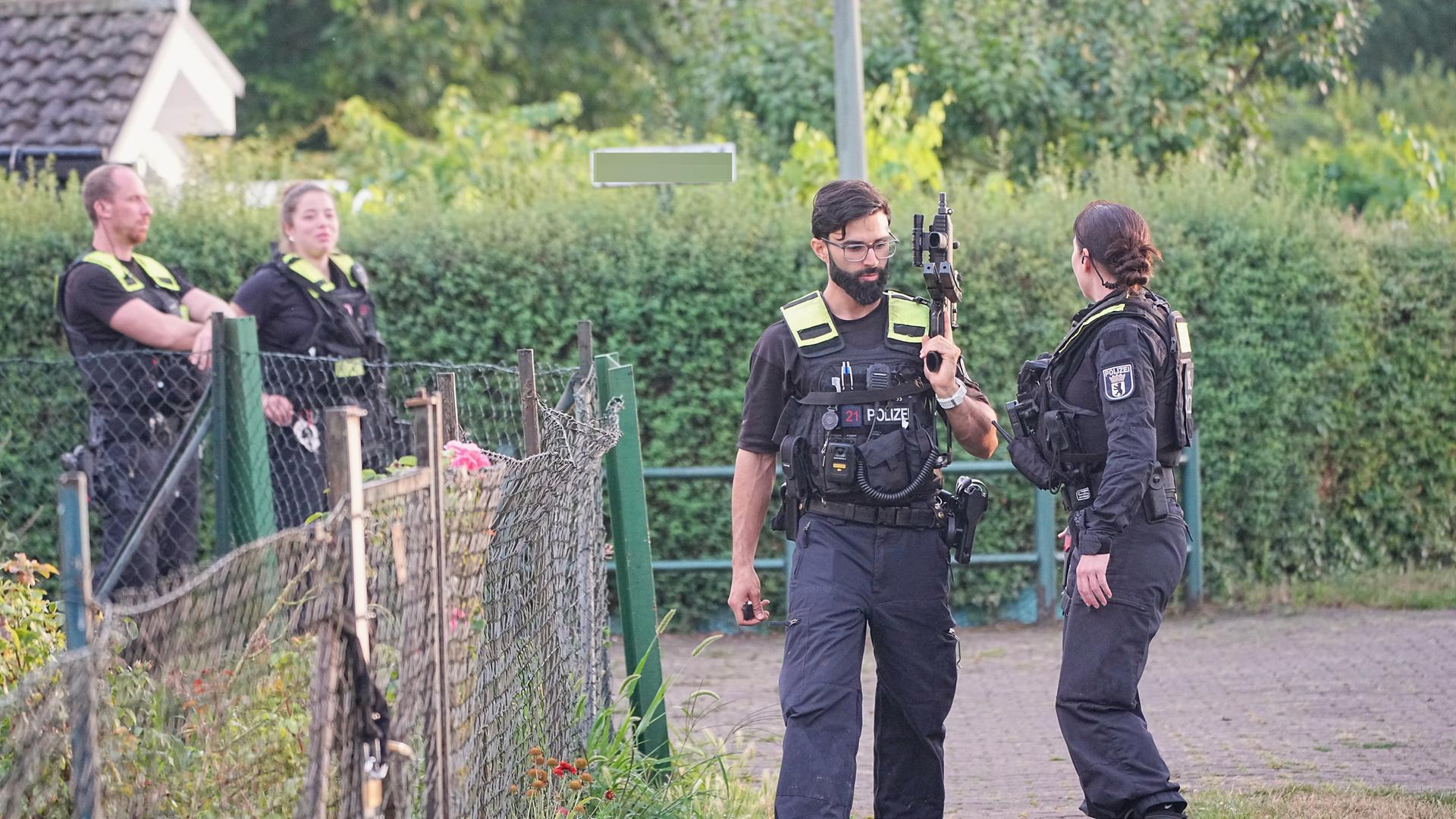 Kräfte der Polizei sind in einer Kleingartenkolonie in Berlin-Spandau im Einsatz und haben Maschinengewehre dabei. 