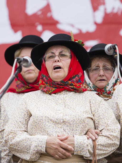 Sängerinnen eines Cante-Alentejano-Chors stehen mit untergehakten Armen vor Mikrofonen und singen. Der Cante Alentejano, der typische Gesang der Provinz Alentejo im Süden Portugals, zählt seit 2014 zum immateriellen UNESCO Weltkulturerbe.