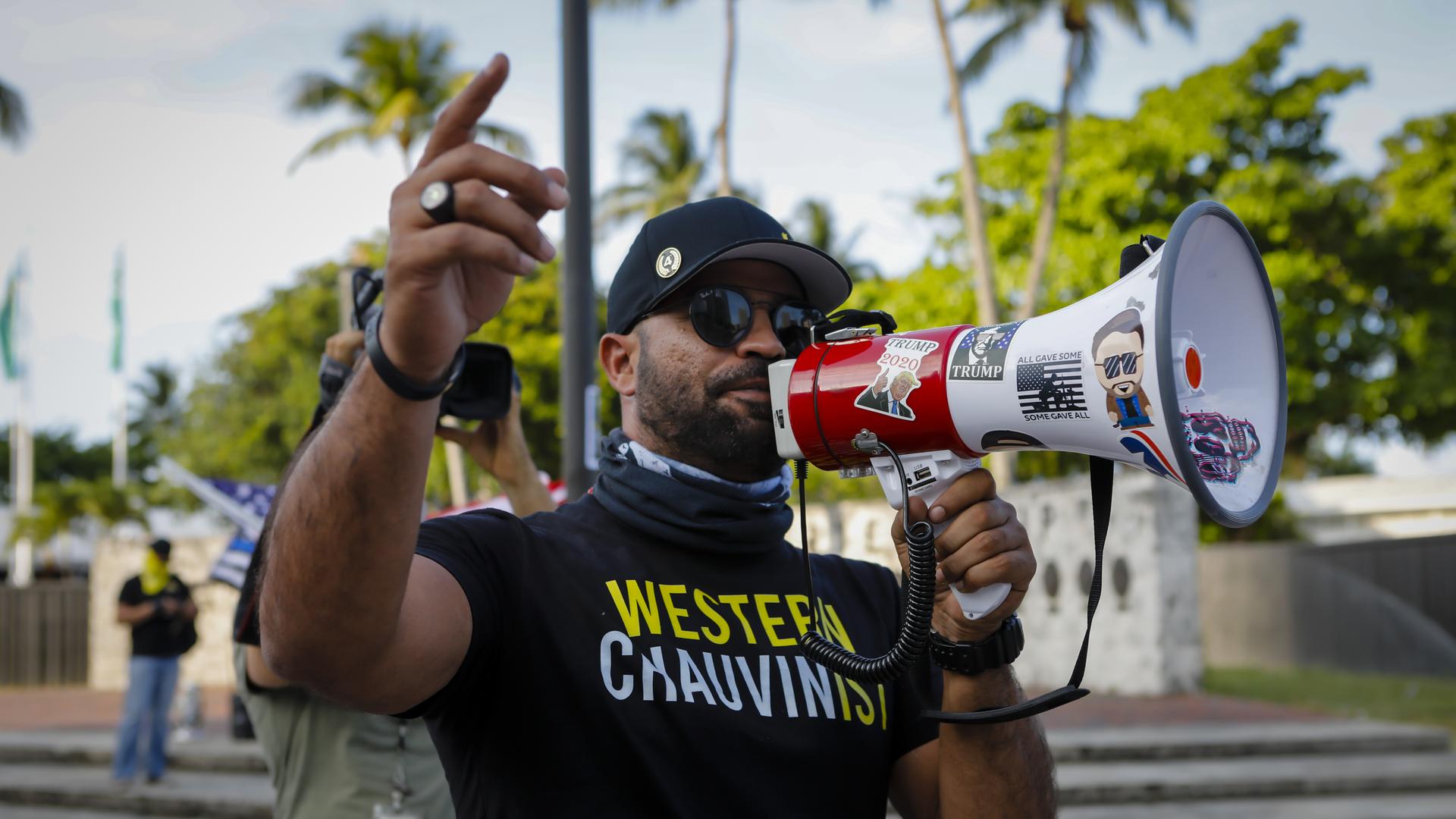 Ein Mann mit einem T-Shirt mit der Aufschrift "Western Chauvinist" spricht in ein mit Trump-Stickern beklebtes Megafon.