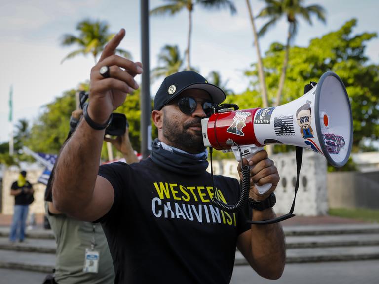 Ein Mann mit einem T-Shirt mit der Aufschrift "Western Chauvinist" spricht in ein mit Trump-Stickern beklebtes Megafon.