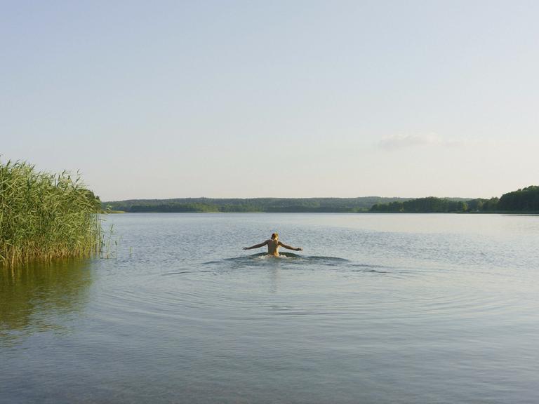 Ein Junge schwimmt alleine in einem sonnigen, ruhigen See in der Uckermark.