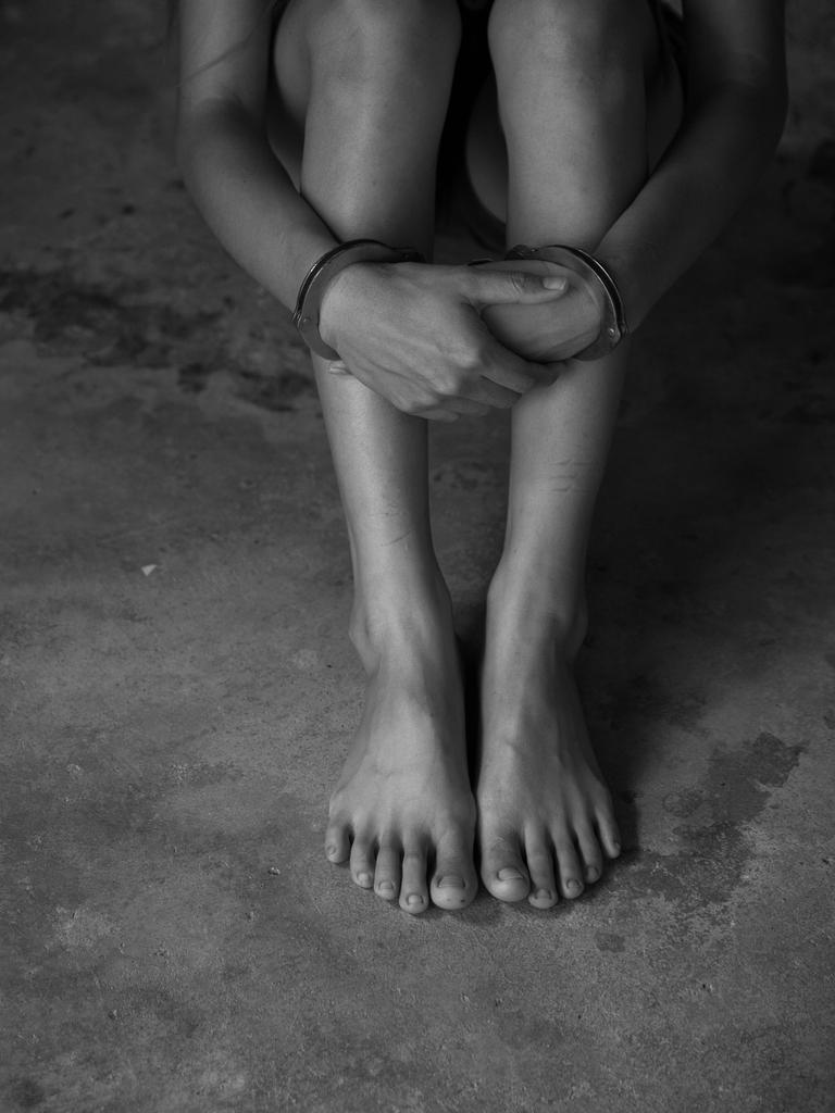 Eine Person sitzt mit Handschellen auf dem Boden. Zu sehen sind nur Arme und Beine. Das Foto ist schwarz-weiss.