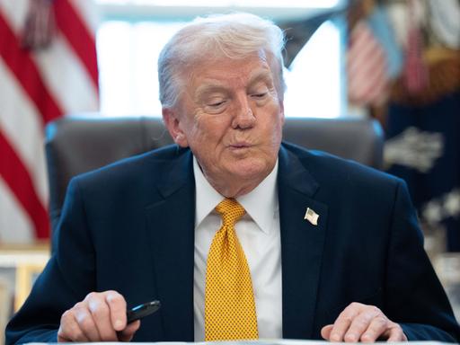 US-Präsident Trump sitzt im Oval Office im Weißen Haus an einem Schreibtisch und verzieht nachdenklich das Gesicht.