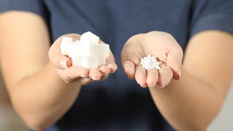 Eine Frau hält Zuckerstückchen in der einen und Süßstoff-Dragees in der anderen Hand
