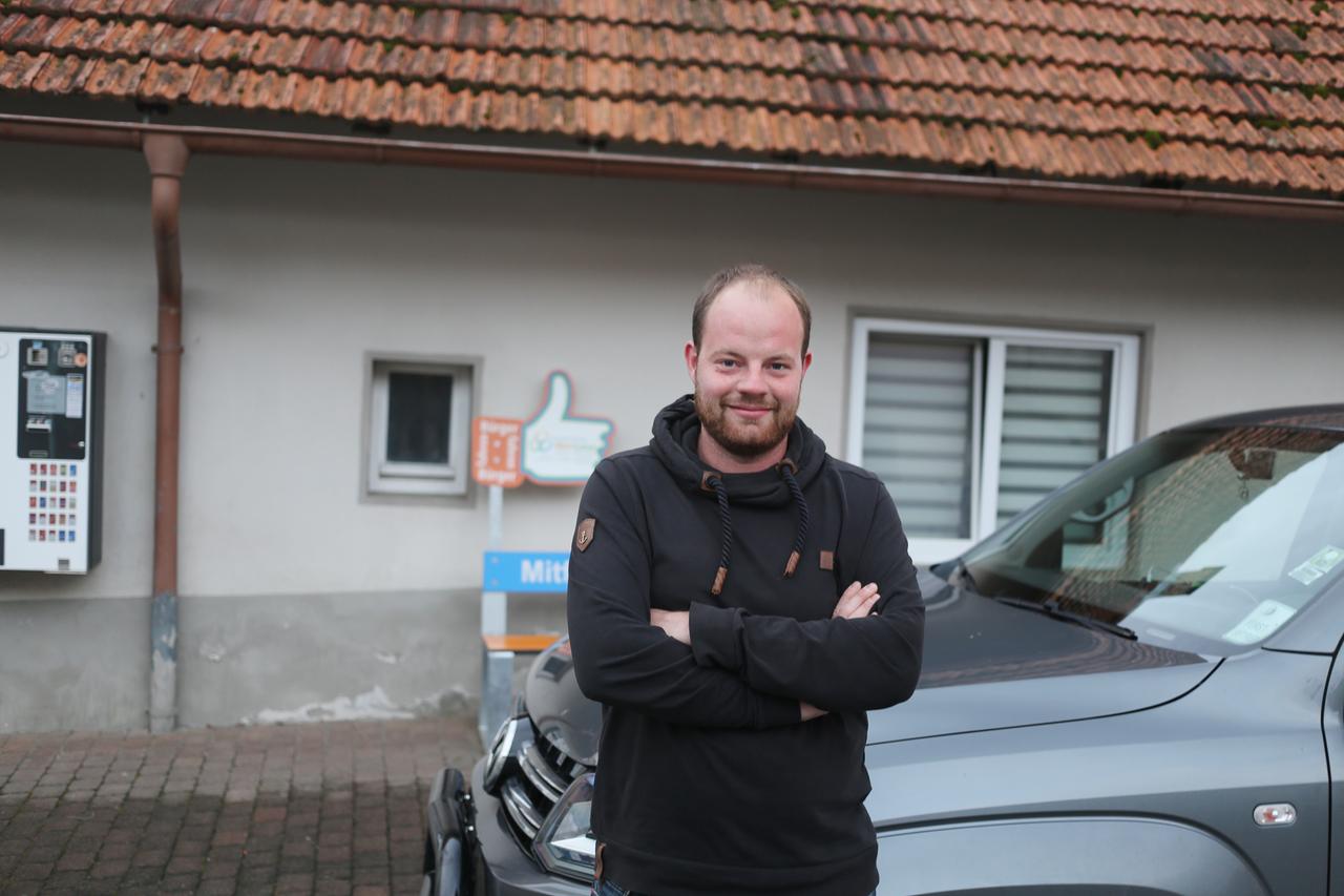 Ein junger Mann steht an ein Pickup angelehnt und schaut in die Kamera.