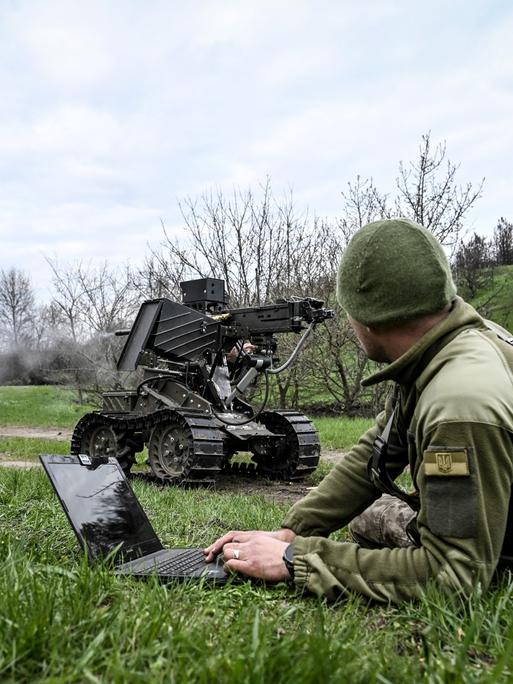 Ein Soldat bedient mit dem Laptop ein Roboterfahrzeug, auf das ein Maschinengewehr montiert wurde.