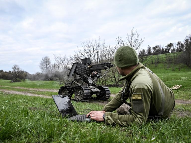 Ein Soldat bedient mit dem Laptop ein Roboterfahrzeug, auf das ein Maschinengewehr montiert wurde.