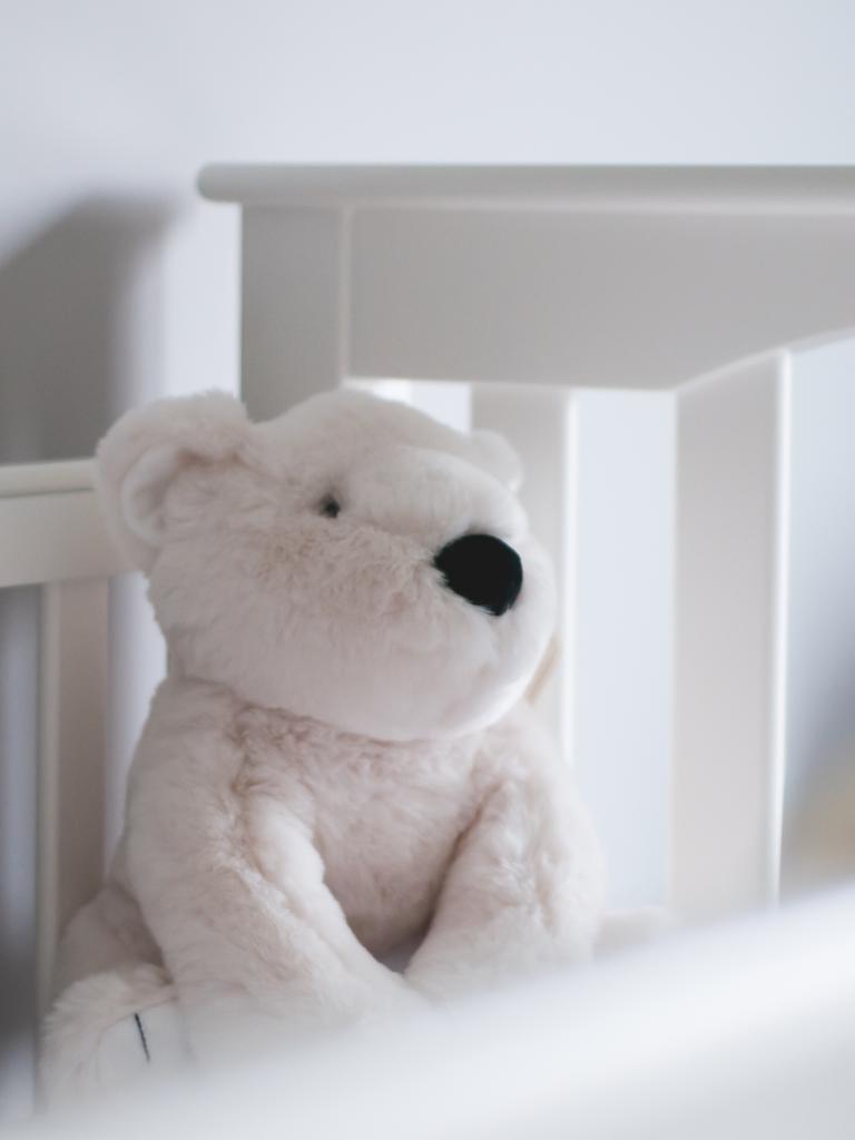 Ein weißer Teddybär sitzt ein einem weißen Kinderbett.