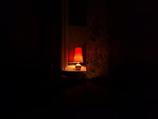Eine kleine Lampe leuchtet in einem Zimmer in die Dunkelheit.