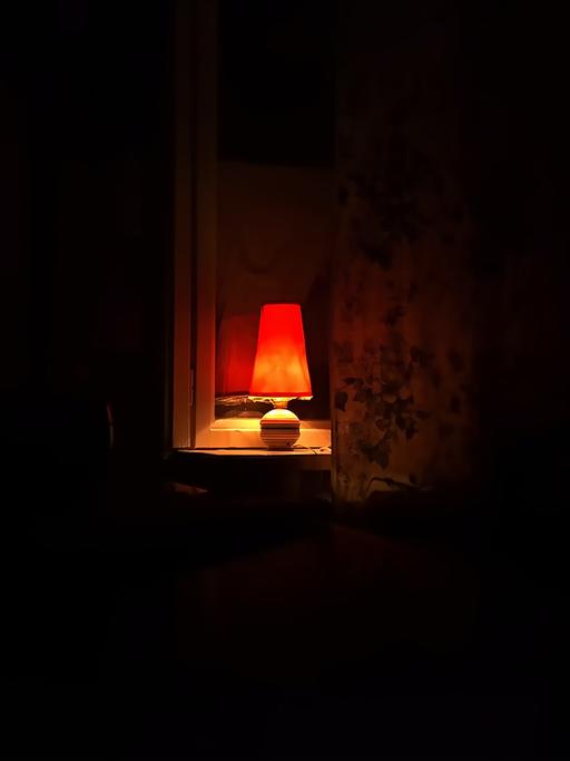 Eine kleine Lampe leuchtet in einem Zimmer in die Dunkelheit.