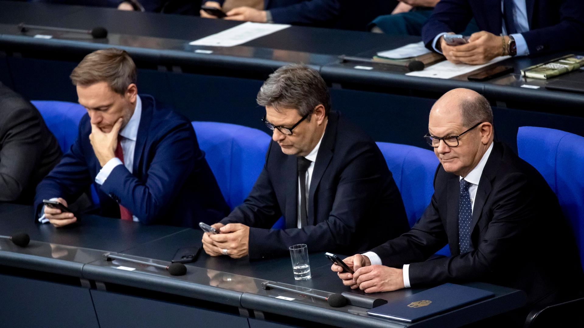 Bundeskanzler Olaf Scholz R, Bundeswirtschaftsminister Robert Habeck C und Bundesfinanzminister Christian Lindner L schauen aufs Handy während der Rede von CDU Vorsitzenden Friedrich Merz im Bundestag in Berlin am 13. Dezember 2023. Plenarsitzung im Bundestag *** Federal Chancellor Olaf Scholz R , Federal Minister of Economics Robert Habeck C and Federal Minister of Finance Christian Lindner L look at their cell phones during the speech of CDU Chairman Friedrich Merz in the Bundestag in Berlin on December 13, 2023 plenary session in the Bundestag