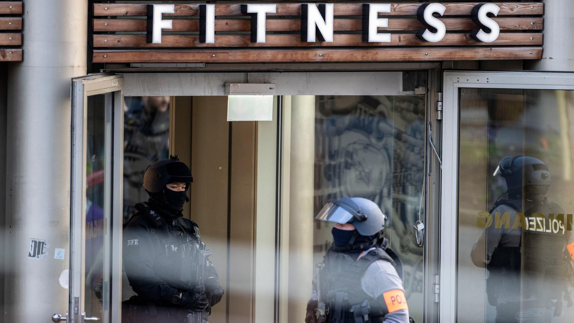 Polizisten mit Helm und Schutzwesten stehen vor einem Gebäude mit der Aufschrift "Fitness".