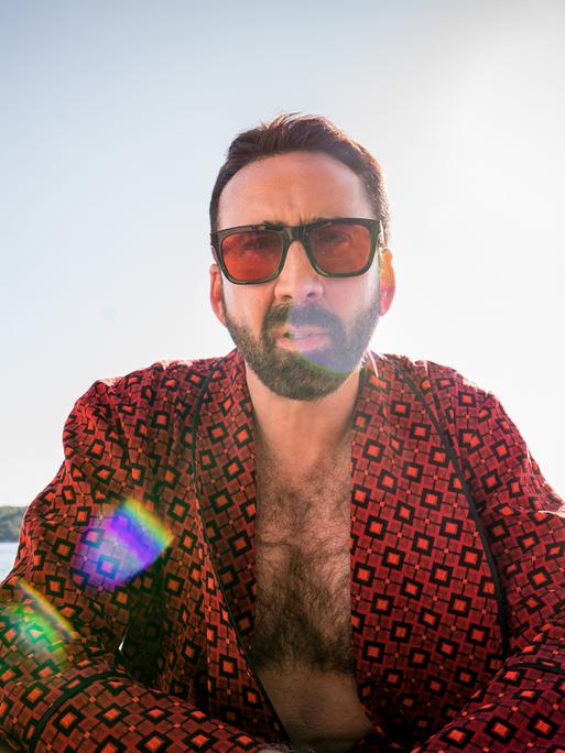 Nicolas Cage sitzt im Gegenlicht scheinbar in einem Boot auf dem Meerm trägt Sonnenbrille und schaut in die Kamera.