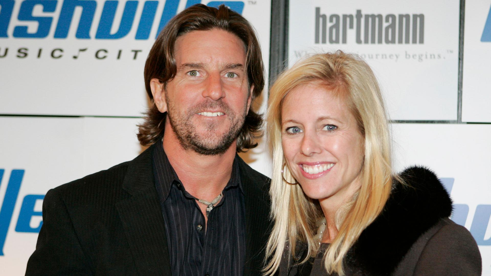 Die beiden stehen nebeneinander vor einer Werbetafel und lächeln in die Kamera. Er hat dunkle Haare und einen Vollbart, sie ist blond. Die beiden stehen nebeneinander vor einer Werbetafel und lächeln in die Kamera. Er hat dunkle Haare und einen Vollbart, sie ist blond.