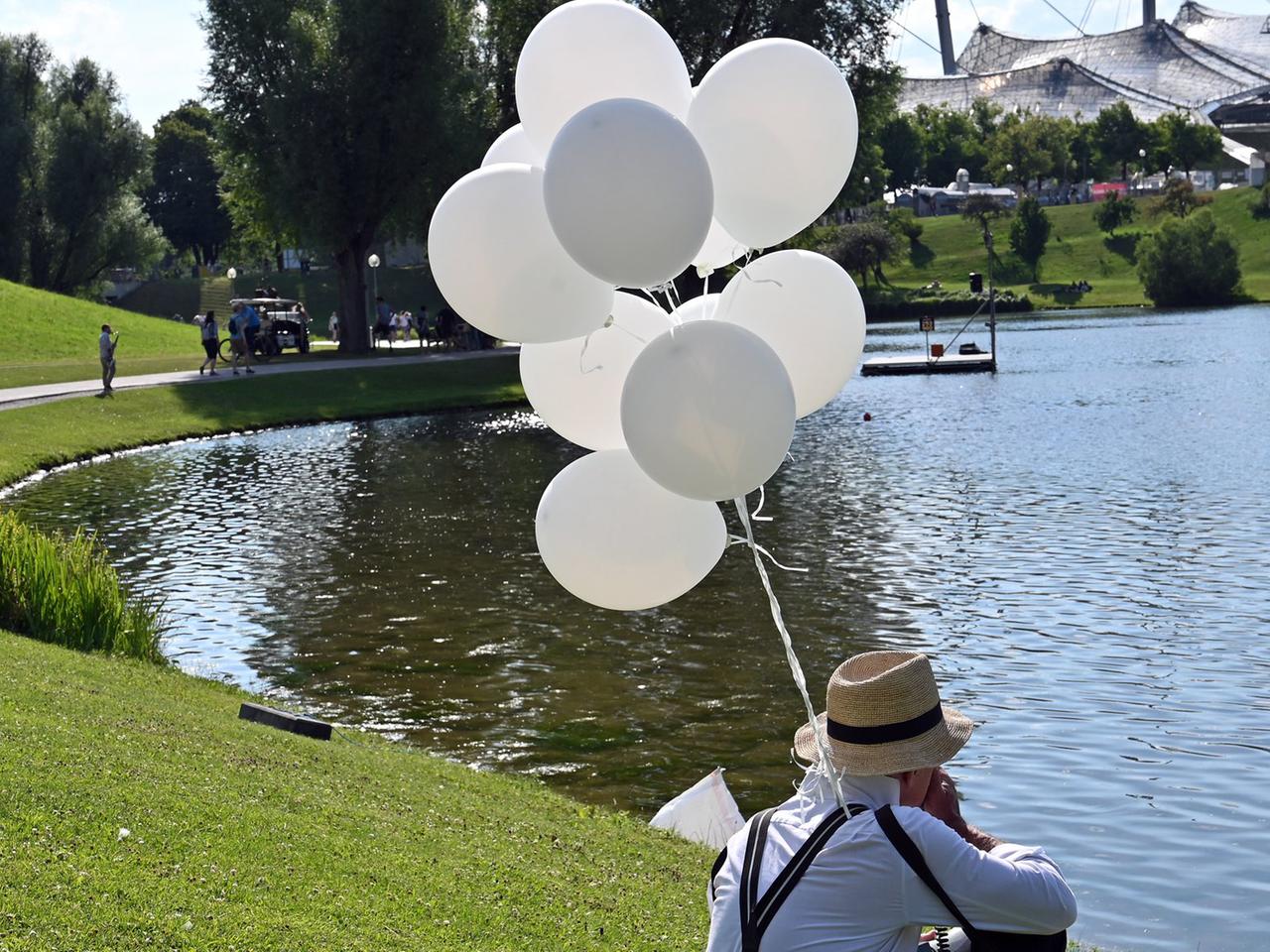 Performance von Stefan Winter. Zu sehen: Stefan Winter mit weißen Lufballons sitzt am See. 