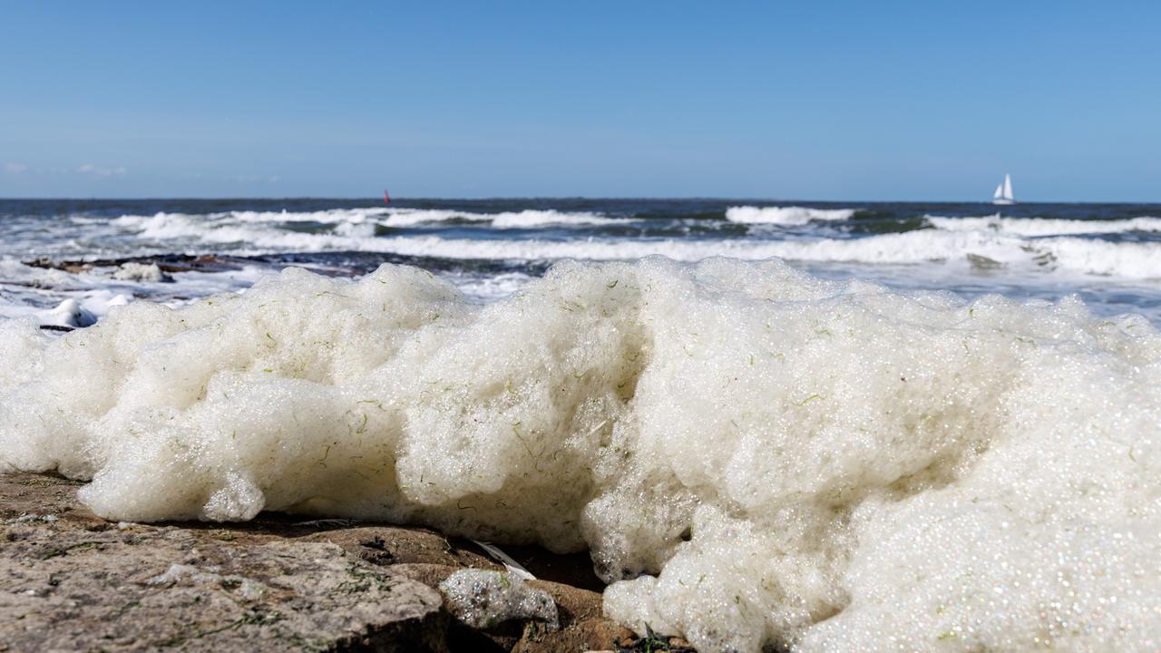 Wellen spülen Schaum an den Strand der ostfriesischen Insel Norderney.