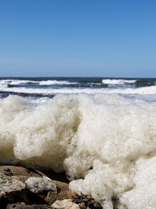 Wellen spülen Schaum an den Strand der ostfriesischen Insel Norderney