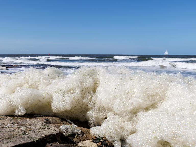Wellen spülen Schaum an den Strand der ostfriesischen Insel Norderney