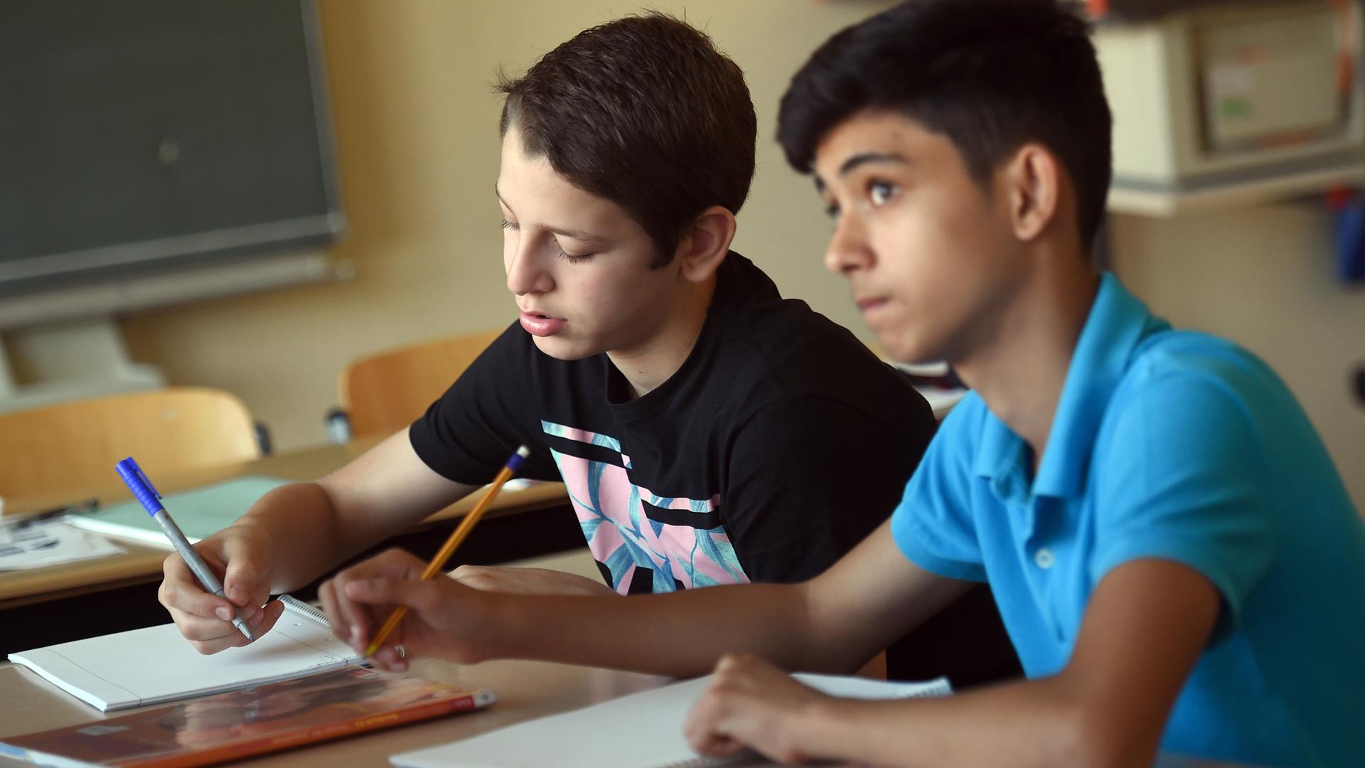 Zwei Schüler sitzen in einem Klassen-Raum und schreiben in einen Block. Zwei Schüler sitzen in einem Klassen-Raum und schreiben in einen Block.
