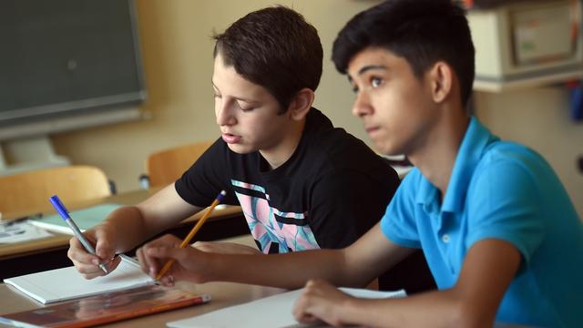 Zwei Schüler sitzen in einem Klassen-Raum und schreiben in einen Block.