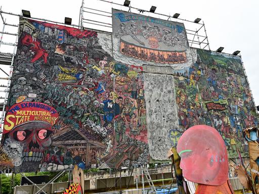 Auf dem etwa 10 x 10 Meter großen Bild der indonesischen Künstlergruppe Taring Padi ist ein Gewimmel verschiedenster Figuren zu sehen, links unten ein Totenkopf und auf dessen Kopfbedeckung die Aufschrift "The Expansion of Multicultural State Hegemony". Auf dem etwa 10 x 10 Meter großen Bild der indonesischen Künstlergruppe Taring Padi ist ein Gewimmel verschiedenster Figuren zu sehen, links unten ein Totenkopf und auf dessen Kopfbedeckung die Aufschrift "The Expansion of Multicultural State Hegemony".