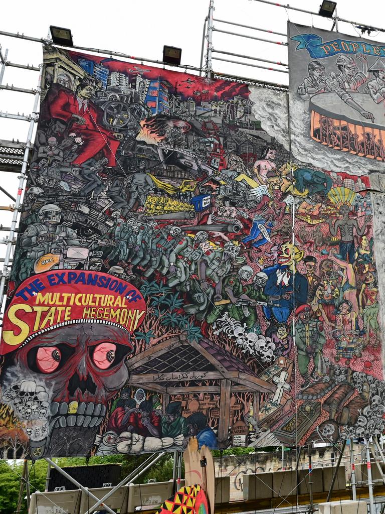 Auf dem etwa 10 x 10 Meter großen Bild der indonesischen Künstlergruppe Taring Padi ist ein Gewimmel verschiedenster Figuren zu sehen, links unten ein Totenkopf und auf dessen Kopfbedeckung die Aufschrift "The Expansion of Multicultural State Hegemony". Auf dem etwa 10 x 10 Meter großen Bild der indonesischen Künstlergruppe Taring Padi ist ein Gewimmel verschiedenster Figuren zu sehen, links unten ein Totenkopf und auf dessen Kopfbedeckung die Aufschrift "The Expansion of Multicultural State Hegemony".