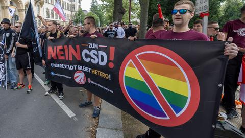 Eine Gruppe Rechtsextremer mit Sonnenbrillen hält ein Banner mit der Aufschrift "Nein zum CSD!" in die Luft. Neben dem Satz steht eine durchgestrichene Regenbogenflagge.