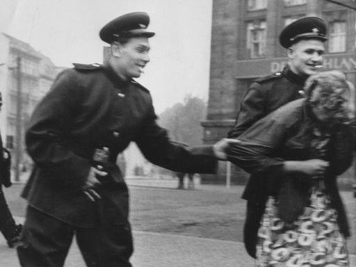 Historisches Schwarzweißfoto von zwei sowjetische Soldaten, die auf der Straße in Leipzig eine Passantin belästigen.