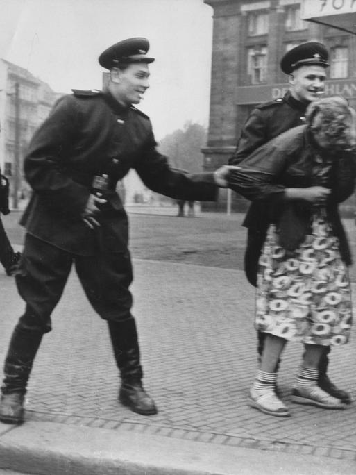 Historisches Schwarzweißfoto von zwei sowjetische Soldaten, die auf der Straße in Leipzig eine Passantin belästigen.