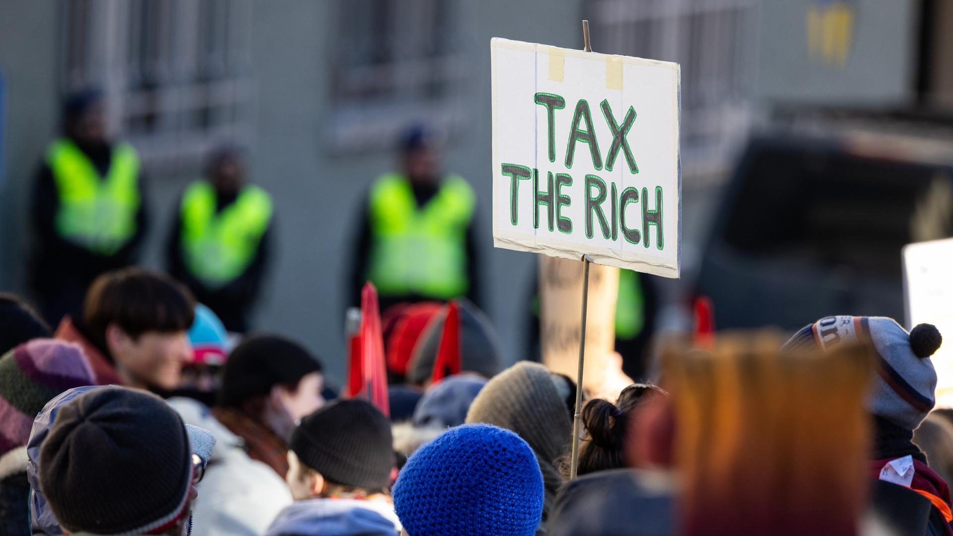 Ein Teilnehmer einer Demonstration in Davos in der Schweiz hält ein Schild, auf dem "Tax the rich" steht. Ein Teilnehmer einer Demonstration in Davos in der Schweiz hält ein Schild, auf dem "Tax the rich" steht.