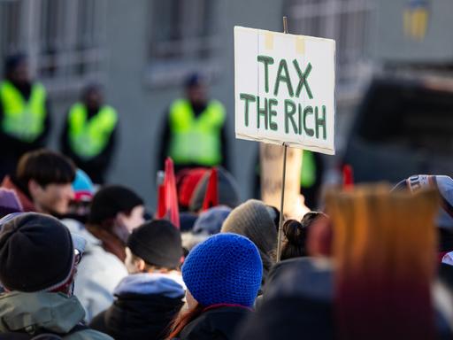 Ein Teilnehmer einer Demonstration in Davos in der Schweiz hält ein Schild, auf dem "Tax the rich" steht.