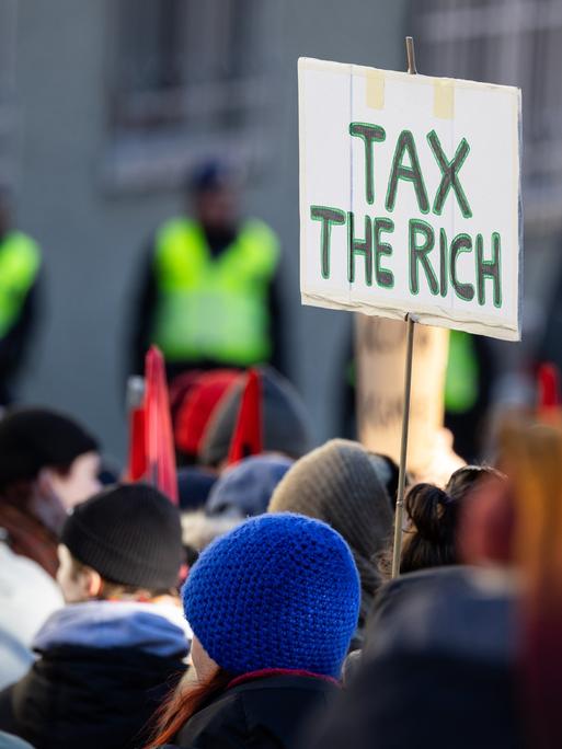 Ein Teilnehmer einer Demonstration in Davos in der Schweiz hält ein Schild, auf dem "Tax the rich" steht.
