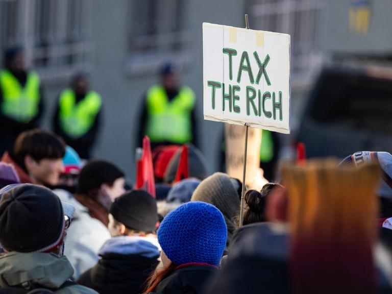 Ein Teilnehmer einer Demonstration in Davos in der Schweiz hält ein Schild, auf dem "Tax the rich" steht.