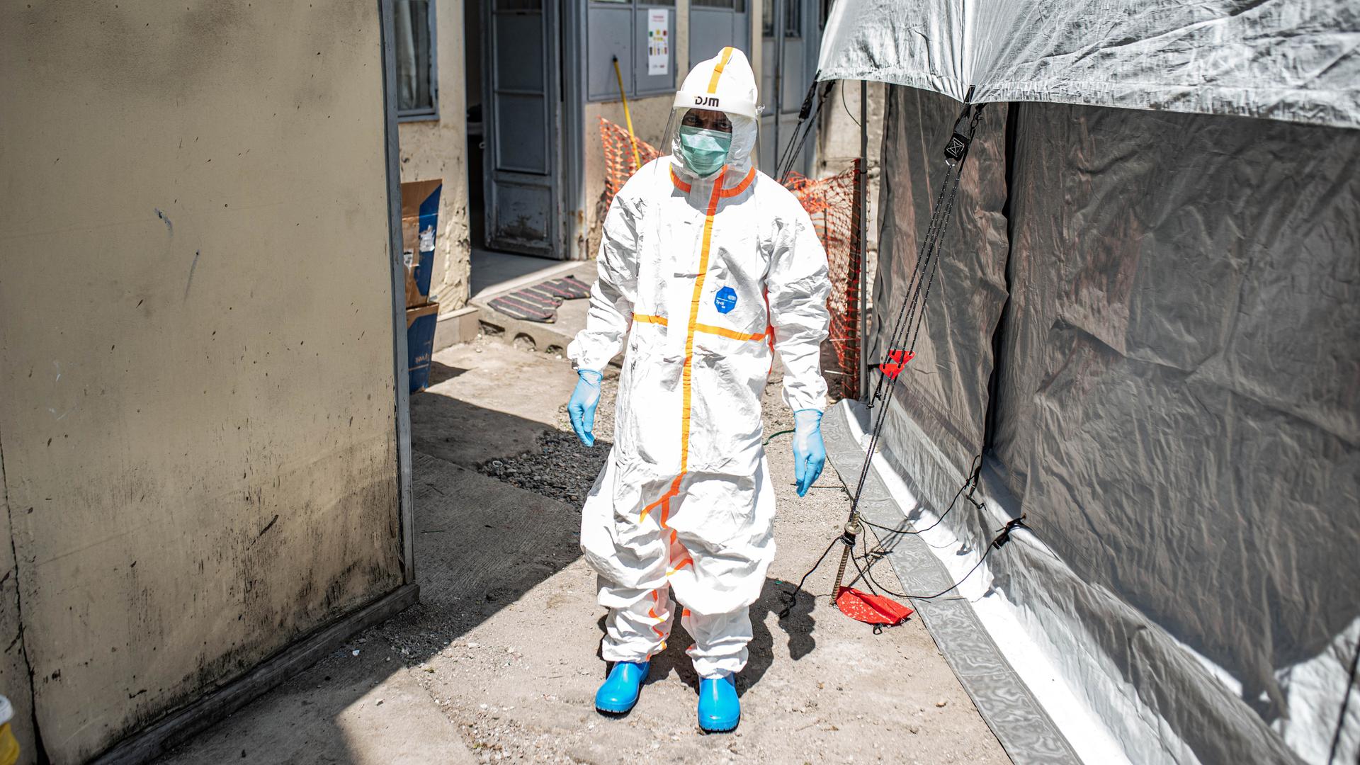 Ein Mitarbeiter reinigt ein Ebola-Behandlungszentrum in Goma (Kongo). Er trägt weiße Schutzkleidung und läuft zwischen zwei Zelten durch.