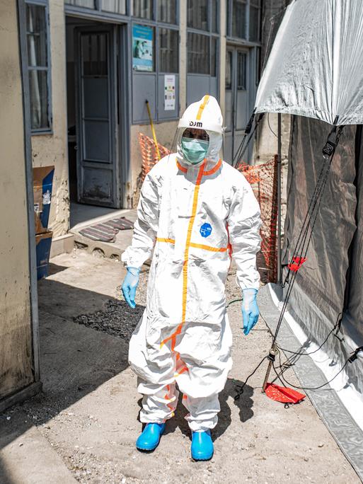Ein Mitarbeiter reinigt ein Ebola-Behandlungszentrum in Goma (Kongo). Er trägt weiße Schutzkleidung und läuft zwischen zwei Zelten durch.
