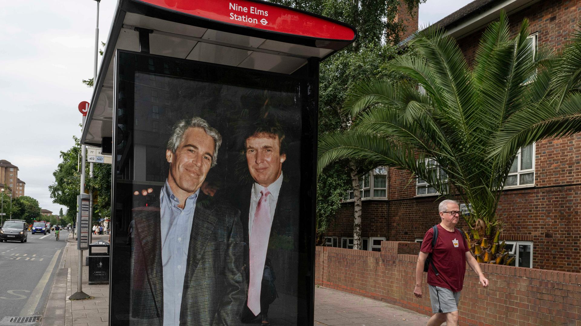 An einer Bushaltestelle hat ein Aktivist ein großformatiges Foto aus den 90er Jahren von Jeffrey Epstein und Donald Trump aufgehängt, dass die beiden freundschaftlich zugewandt zeigt.