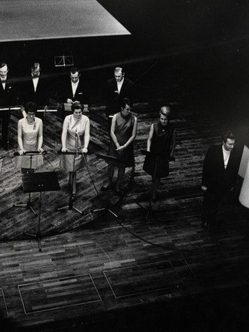 Die Damen und Herren der Schola Cantorum stehen auf der Bühne neben dem Leiter des Ensembles, Clytus Gottwald.