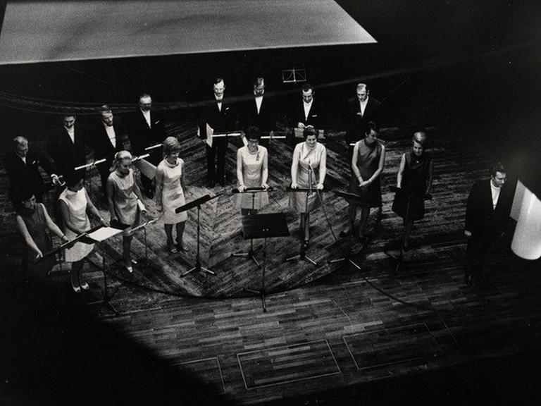 Die Damen und Herren der Schola Cantorum stehen auf der Bühne neben dem Leiter des Ensembles, Clytus Gottwald.
